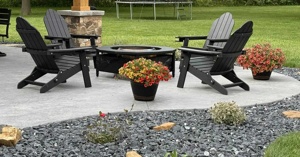 Built-in circular stone fire pit with curved seating wall and paver patio surround at dusk